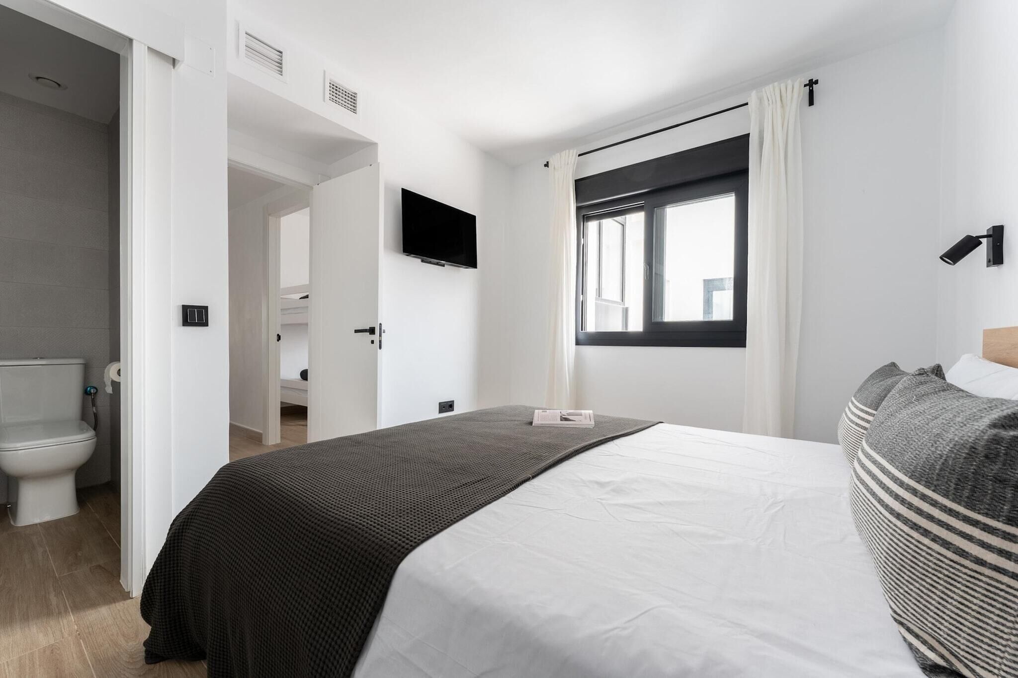 Ein modernes Hotelzimmer mit einem großen Bett, einem Flachbildfernseher, einem Fenster mit Vorhängen und einem durchgegangene Tür erkennbaren Badezimmer.