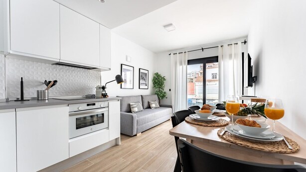 Una cocina moderna con armarios blancos, un sofá gris y una zona de comedor con desayuno listo.