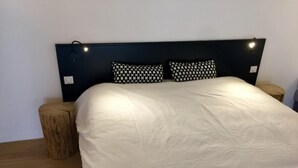 Ein Bett mit weißer Daunendecke, zwei Kissen mit Schwarz-Weiß-Muster und einem dunklen Kopfteil. Auf beiden Seiten des Bettes befinden sich jeweils Nachttische mit Lampen.