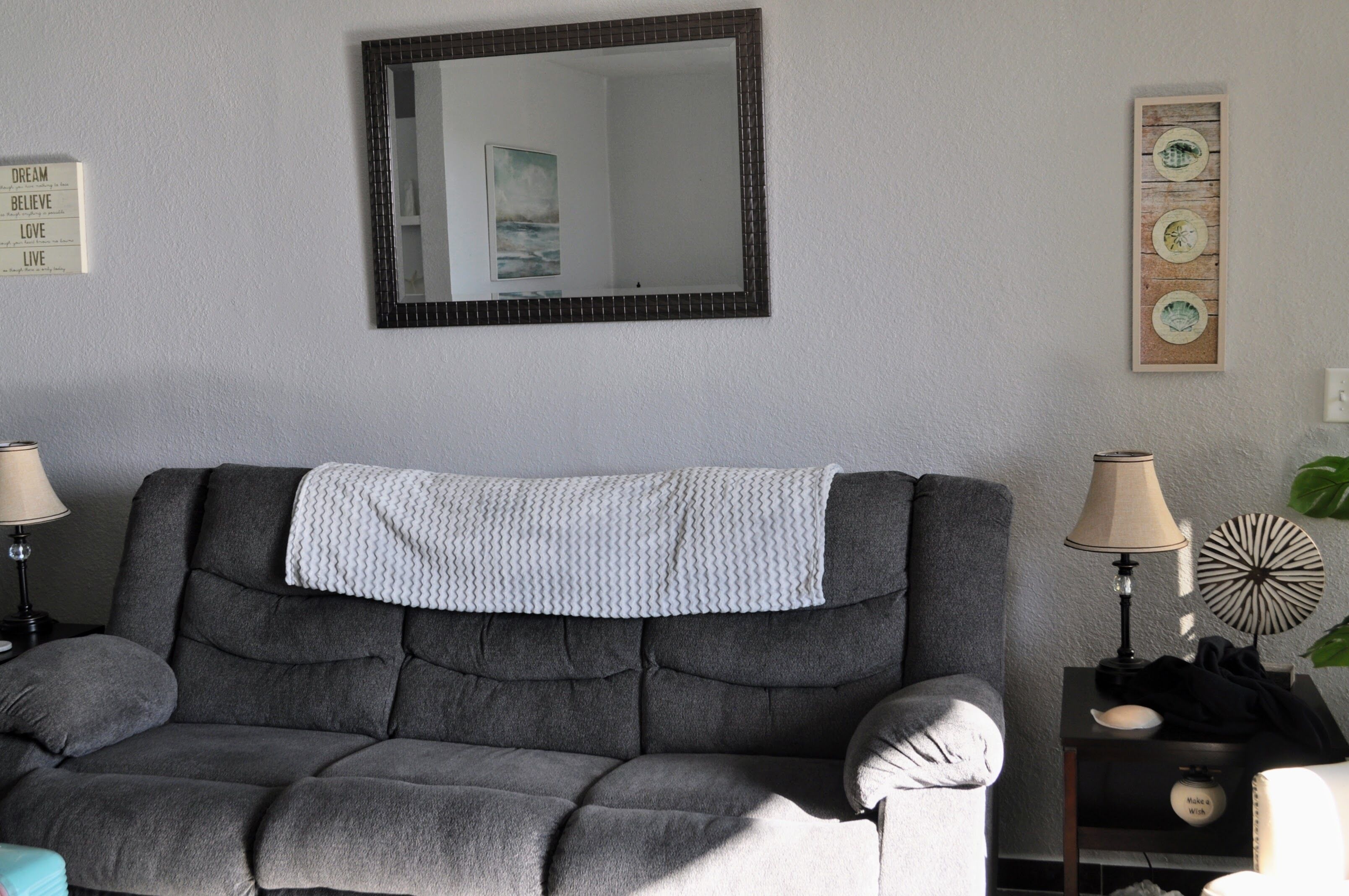 Ein Wohnzimmer mit grauem Sofa, einem Spiegel, einem Wandbild und einem kleinen Tisch mit einer Lampe.