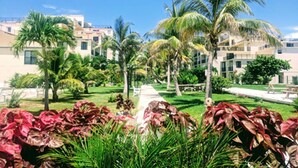 A hotel with multiple floors, palm trees, and a well-maintained garden with red-leafed plants. - Coral Beach Retreat. Garden view. Steps from pool & beach. 1 mile to Port Lucaya (Freeport)