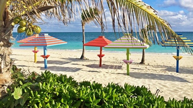 A beach with colorful striped umbrellas and palm trees. - Coral Beach Retreat. Garden view. Steps from pool & beach. 1 mile to Port Lucaya (Freeport)