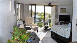 A hotel room with a balcony, a sofa, a chair, a bed, a TV, and a fan. - Coral Beach Retreat. Garden view. Steps from pool & beach. 1 mile to Port Lucaya (Freeport)