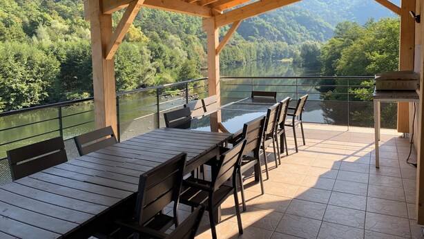 Un área de comedor al aire libre, techada, con una mesa y sillas, con vista a un río y colinas arboladas.