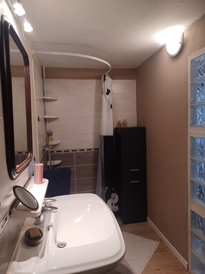 Ein Badezimmer mit weißem Waschbecken, Spiegel und Duschbereich.