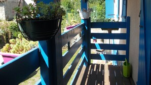 A balcony with a blue railing, a hanging planter with green plants, and a view of houses in the background.