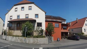 Un immeuble à plusieurs étages doté d’un balcon au rez-de-chaussée, d’un escalier menant aux étages supérieurs et d’une voiture garée devant.