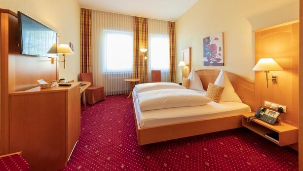Une chambre d’hôtel comprenant un lit, une table de chevet, une lampe, un bureau, une chaise et une petite table avec un téléphone.