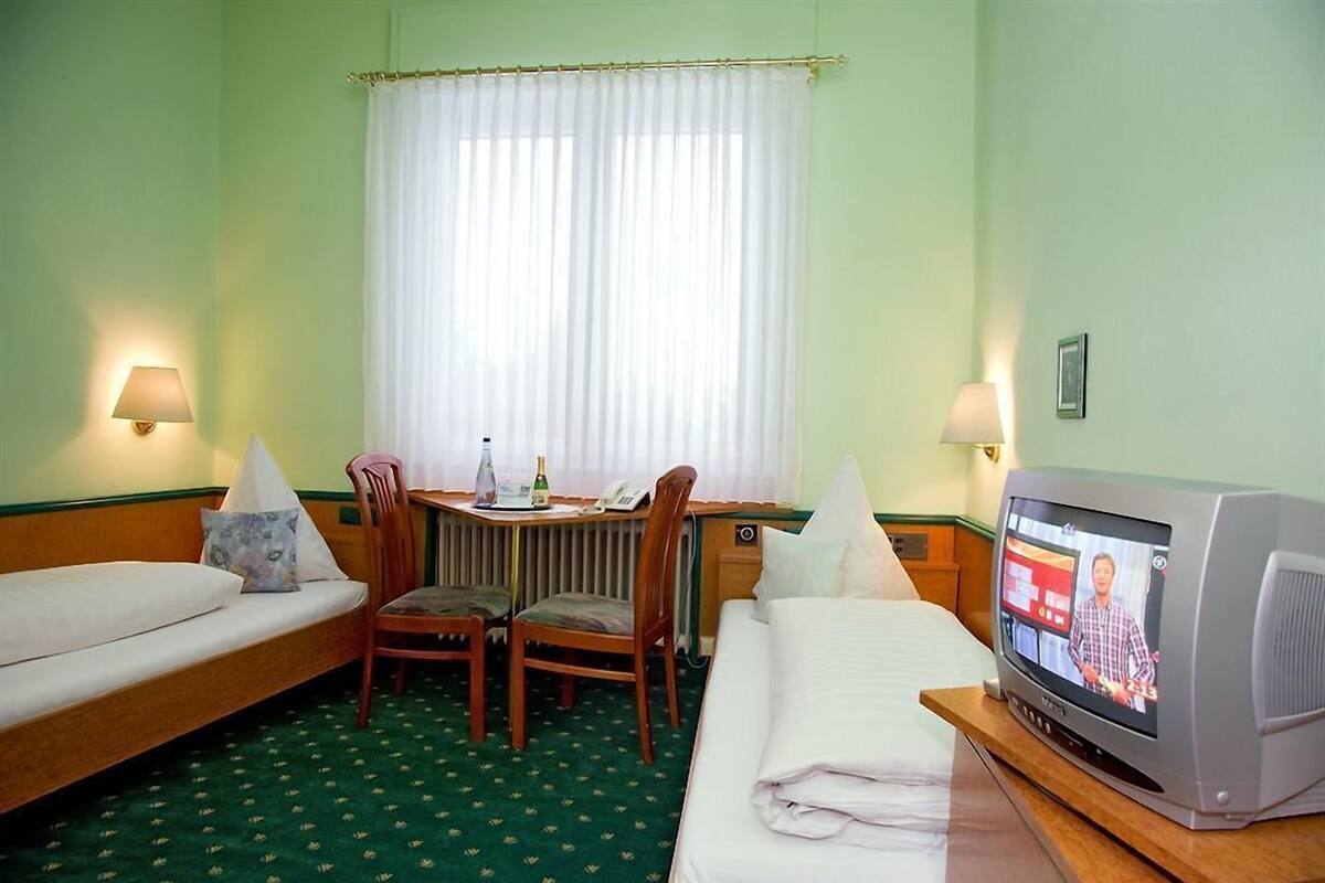A hotel room with a bed, a desk with a chair, a television, and a window with curtains.