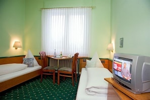 A hotel room with a bed, a desk with a chair, a television, and a window with curtains.