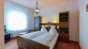 Une chambre d’hôtel avec un lit en bois, une table de chevet, une armoire et un lustre.