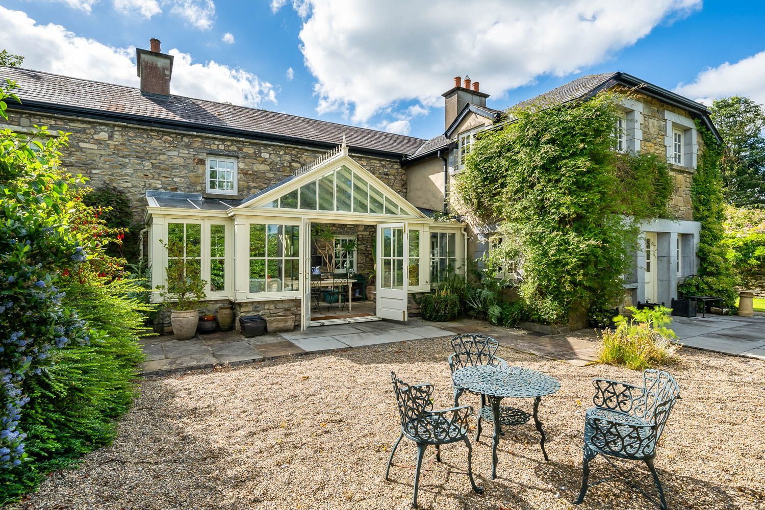 A stone house with a conservatory, a gravel patio, and metal outdoor furniture.