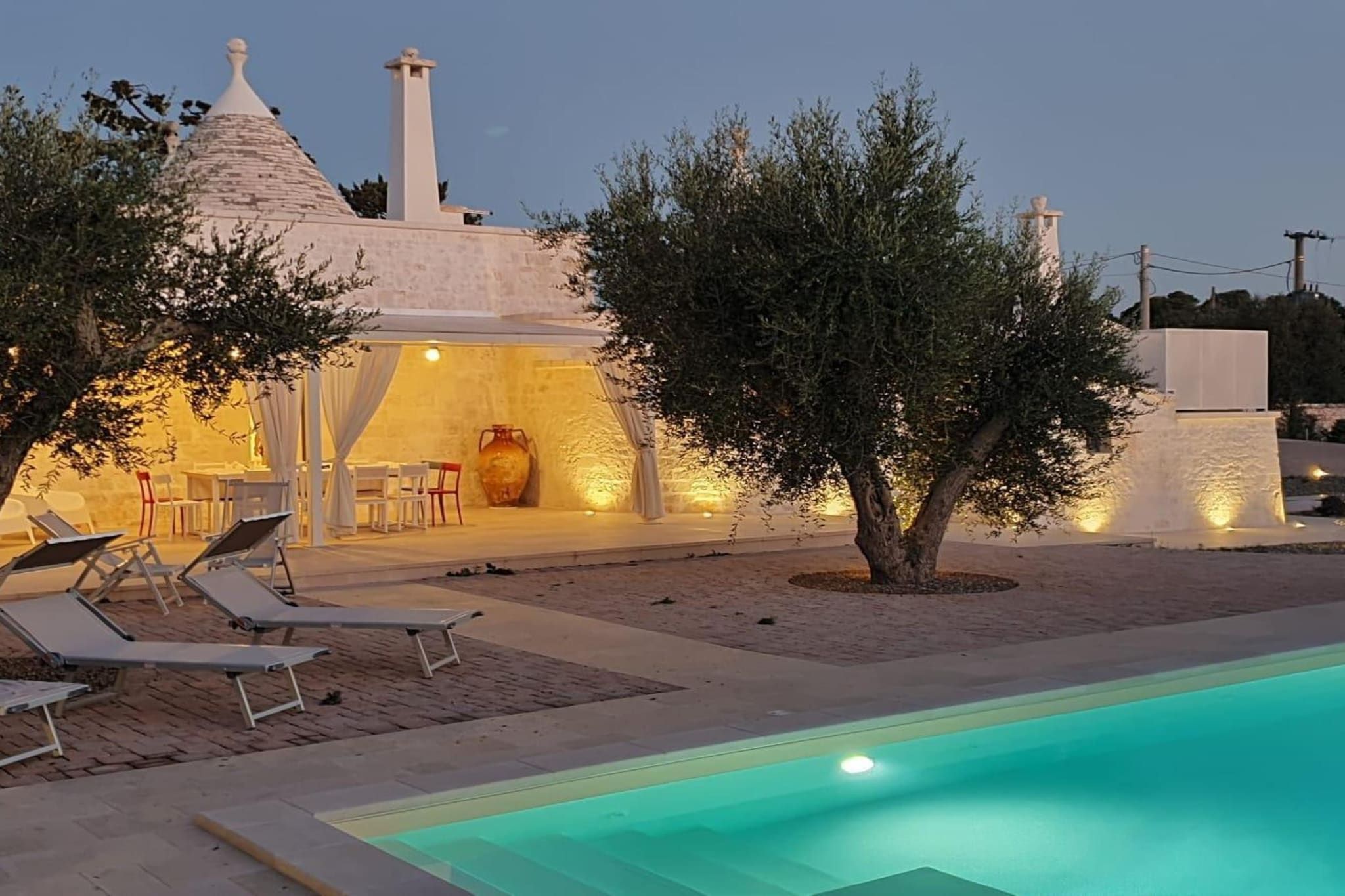 A villa with a swimming pool, outdoor seating, and a well-lit interior.
