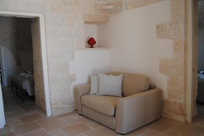 A room with a beige sofa, two striped pillows, and a red decorative item on a shelf.