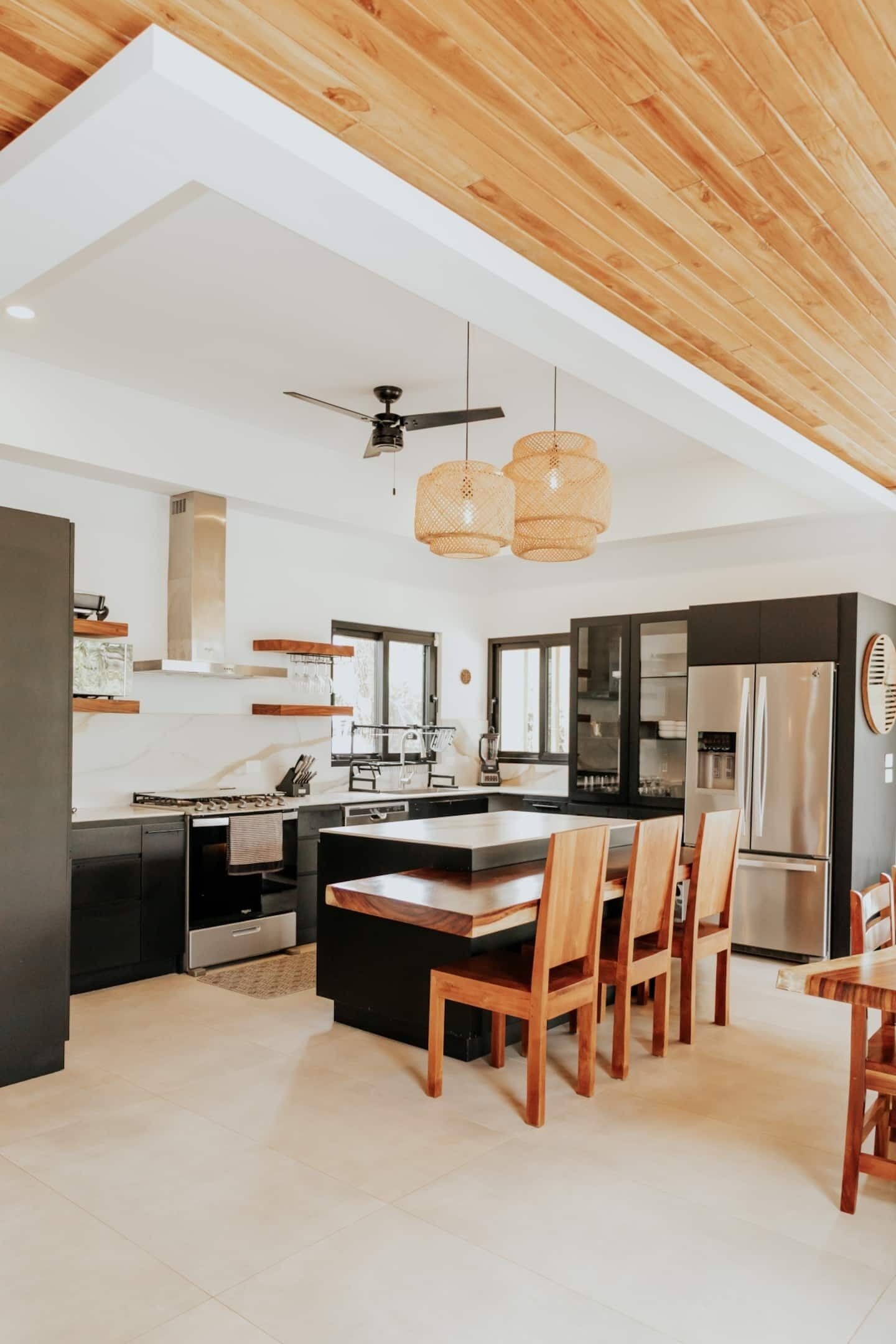 A modern kitchen with a central island, wooden chairs, and a ceiling fan.