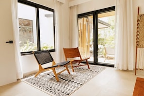 Una habitación con dos sillas de madera, un tapete estampado y ventanas grandes con cortinas.