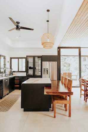 Una cocina moderna con una isla central, electrodomésticos integrados y una zona de comedor con sillas de madera.