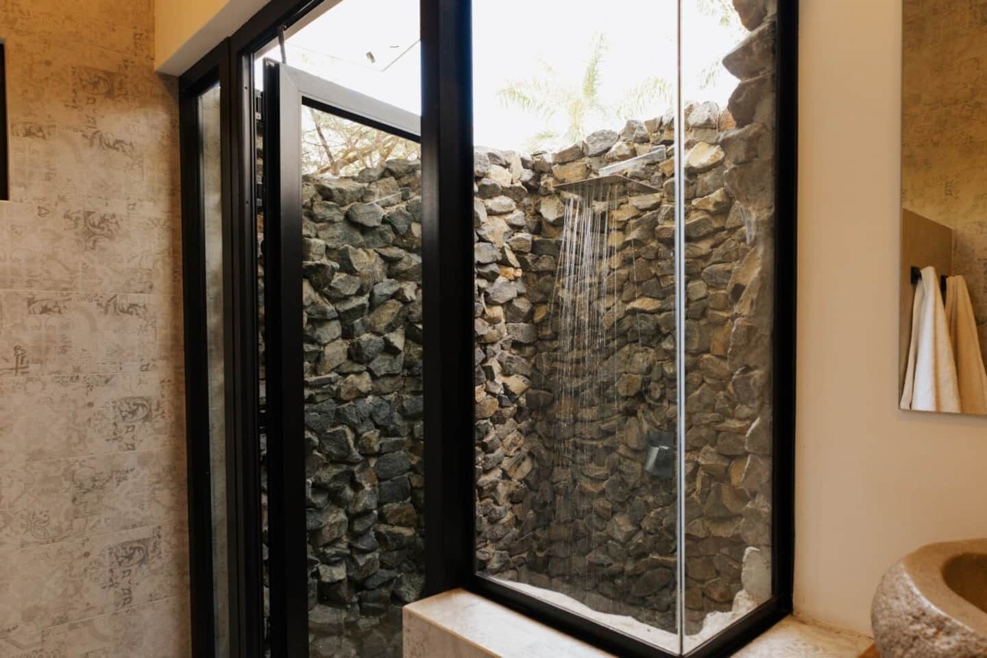 Un bagno con parete in pietra, cabina doccia in vetro e lavabo in pietra.