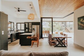 Una cocina moderna con una isla central, comedor con mobiliario de madera y grandes ventanas con vistas al exterior.