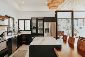 Una cocina moderna con una isla central, armarios negros, electrodomésticos de acero inoxidable y una zona de comedor con mobiliario de madera.
