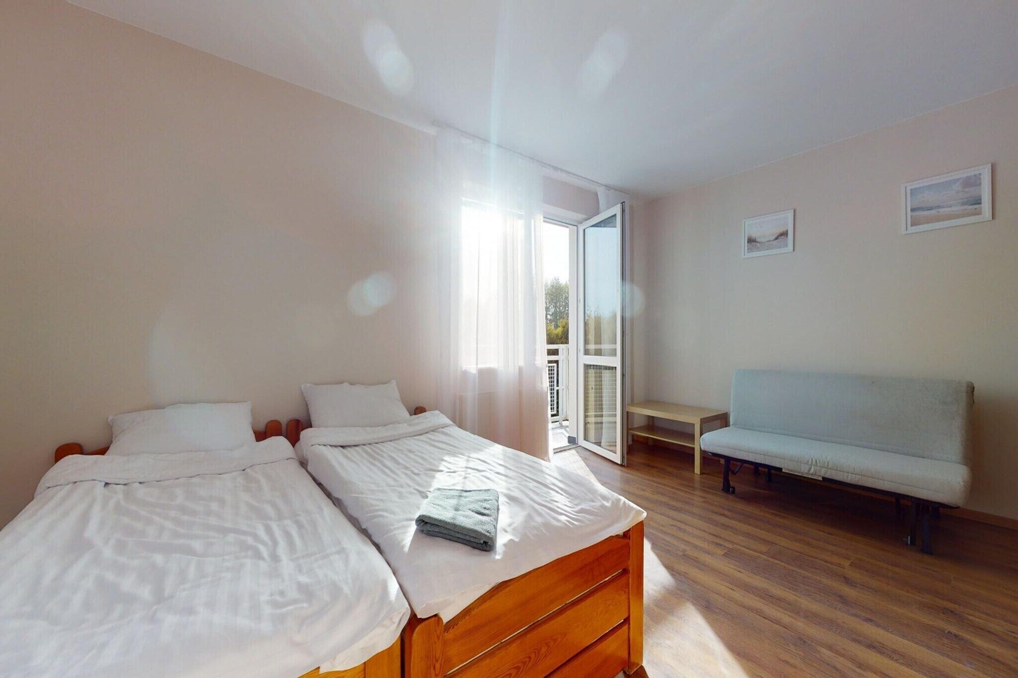 A bedroom with two beds, a bench, and a balcony door.