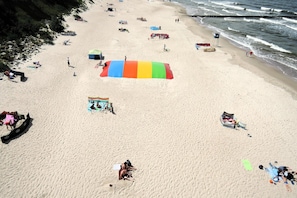 A beach with people sunbathing, a large colorful umbrella, and a rocky shoreline.
