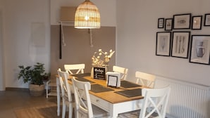 A dining area with a wooden table and white chairs, a hanging light fixture, and framed pictures on the wall. - TKS HOME Am Weiherplatz In the heart of the Westerwald (Norken)