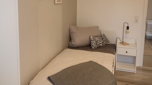 A small, neatly arranged bedroom with a bed, a bedside table, a lamp, and a TV mounted on the wall. - TKS HOME Am Weiherplatz In the heart of the Westerwald (Norken)