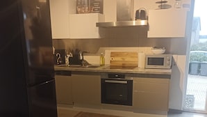 A modern kitchen with a black refrigerator, stainless steel appliances, and a wooden backsplash. - TKS HOME Am Weiherplatz In the heart of the Westerwald (Norken)