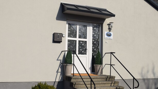 A building with a white exterior, a door with a window, and a set of stone steps leading up to the entrance. - TKS HOME Am Weiherplatz In the heart of the Westerwald (Norken)