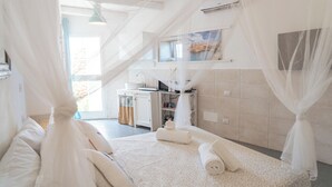 A bedroom with a bed, a bedside table, a window, and a bathroom visible in the background.