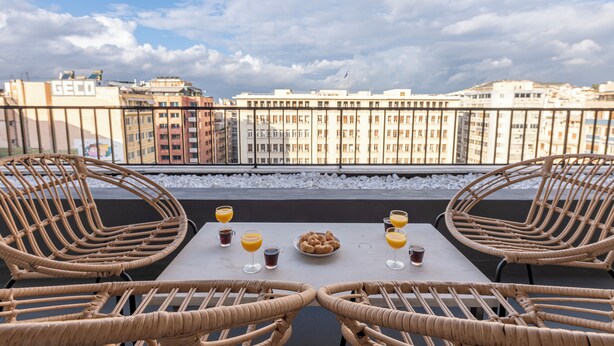 A terrace with wicker chairs, a table with breakfast items, and a city view.