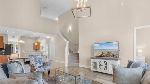 Un salón espacioso con una escalera, un televisor y una cocina al fondo.