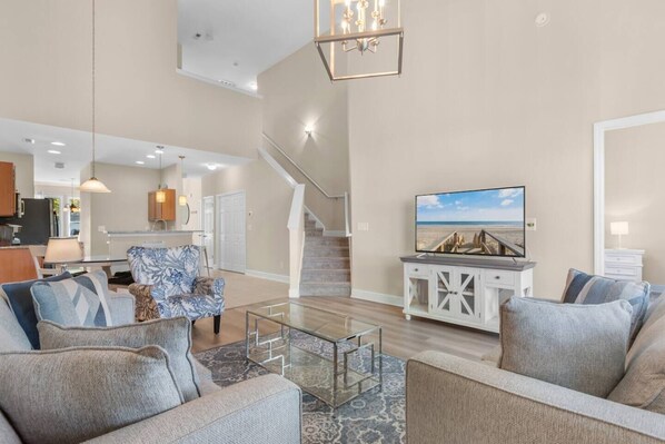 A spacious living room with a staircase, a television, and a kitchen in the background.