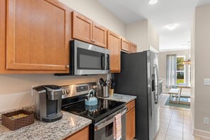A modern kitchen with stainless steel appliances, wooden cabinets, and a granite countertop. - Cozy Barefoot Resort Condo - Pool & Golf (North Myrtle Beach)