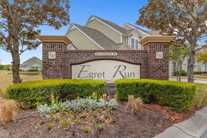A residential building with a brick facade, a sign reading 'Egrett Run,' and a well-maintained lawn with various plants. - Cozy Barefoot Resort Condo - Pool & Golf (North Myrtle Beach)