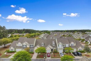 A residential area with multiple two-story houses, each with a front garage, surrounded by trees and a clear sky.