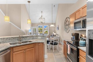 A kitchen with granite countertops, wooden cabinets, stainless steel appliances, and pendant lighting.