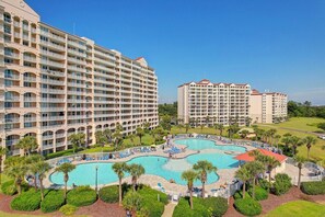 A hotel with multiple balconies, a central swimming pool, and surrounding greenery. - Cozy Barefoot Resort Condo - Pool & Golf (North Myrtle Beach)