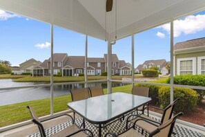 A conservatory with a glass table and chairs, overlooking a residential area with houses and a water body.
