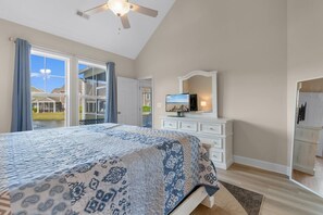 A bedroom with a large bed, a dresser, a television, and a view of the outdoors.