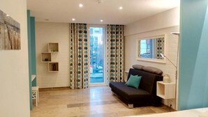 A modern living room with a sofa, a small table, and a window with curtains. - Kabine7 (Koksijde)