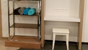 A room with a TV mounted on a white wall, a small white table, and a glass shelf with rolled towels. - Kabine7 (Koksijde)