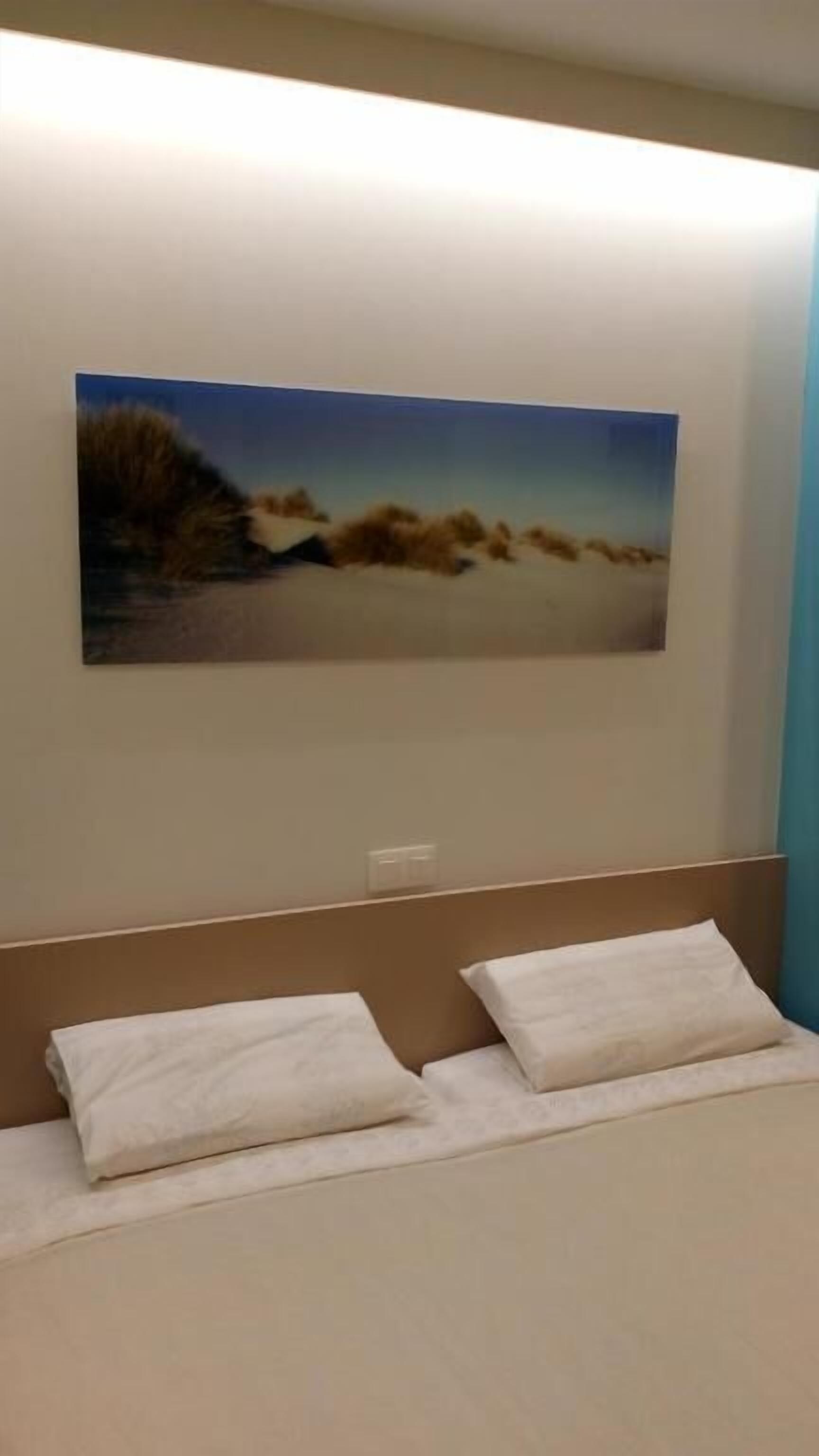 Una camera da letto con un letto, due cuscini e un quadro appeso raffigurante una spiaggia.