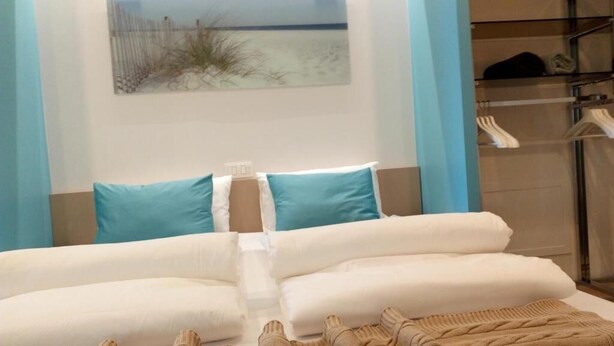 A hotel room with a bed, pillows, a bedside table, and a wall-mounted artwork. - Kabine7 (Koksijde)