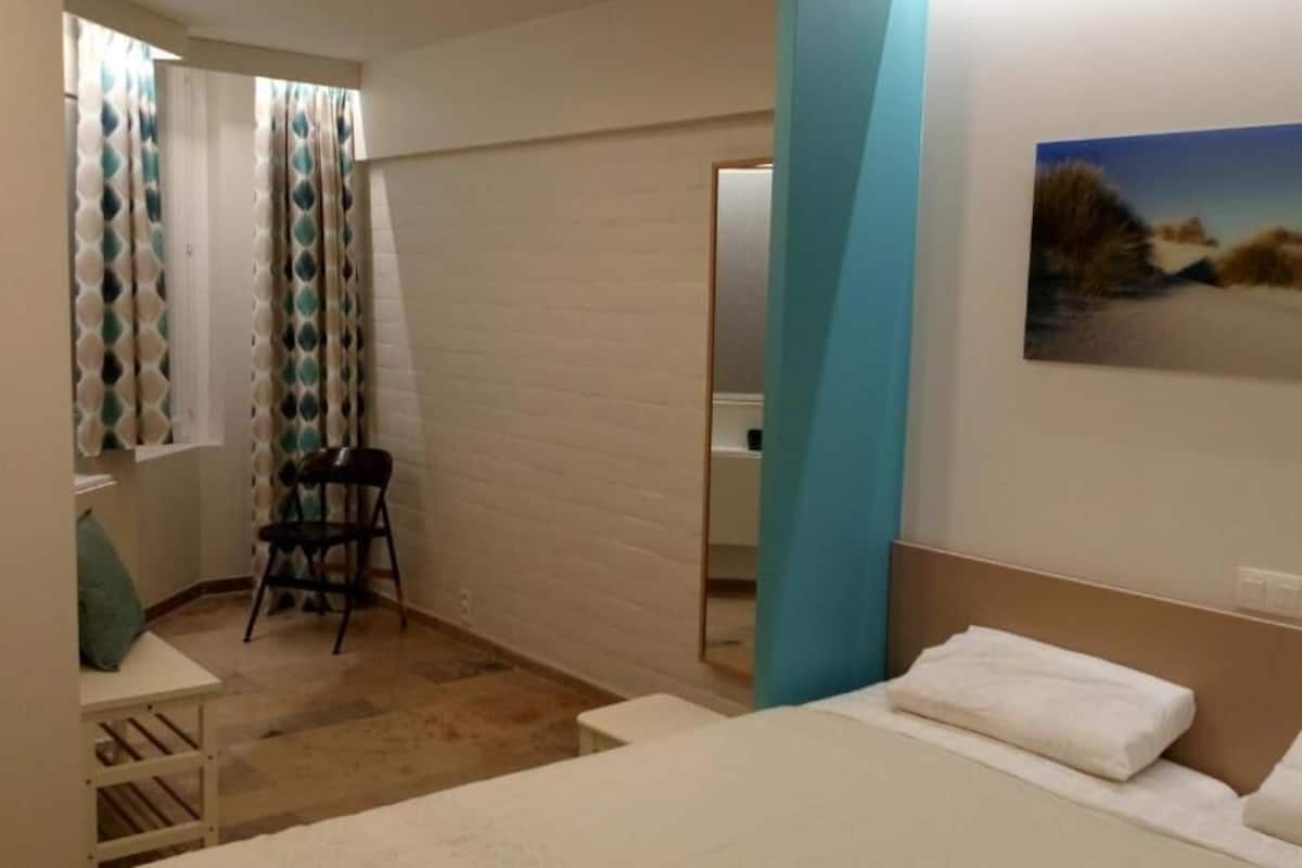 A hotel room with a bed, a chair, a small table, a mirror, and a painting on the wall.