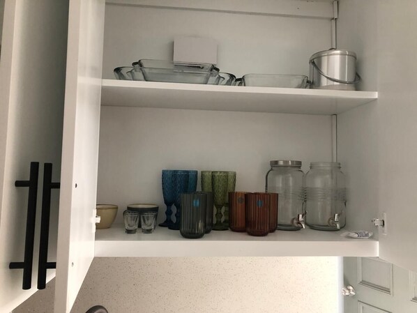 A kitchen with white cabinets, a countertop, and various kitchenware including jars, glasses, and a kettle.