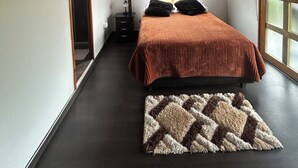 A bedroom with a wooden ceiling, a bed with a striped blanket, a nightstand, and a patterned rug. - Forest House (Salento)