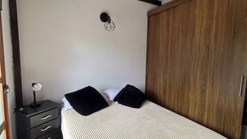 A bedroom with a bed, a wooden wardrobe, a bedside table with a lamp, and a wall-mounted light fixture.