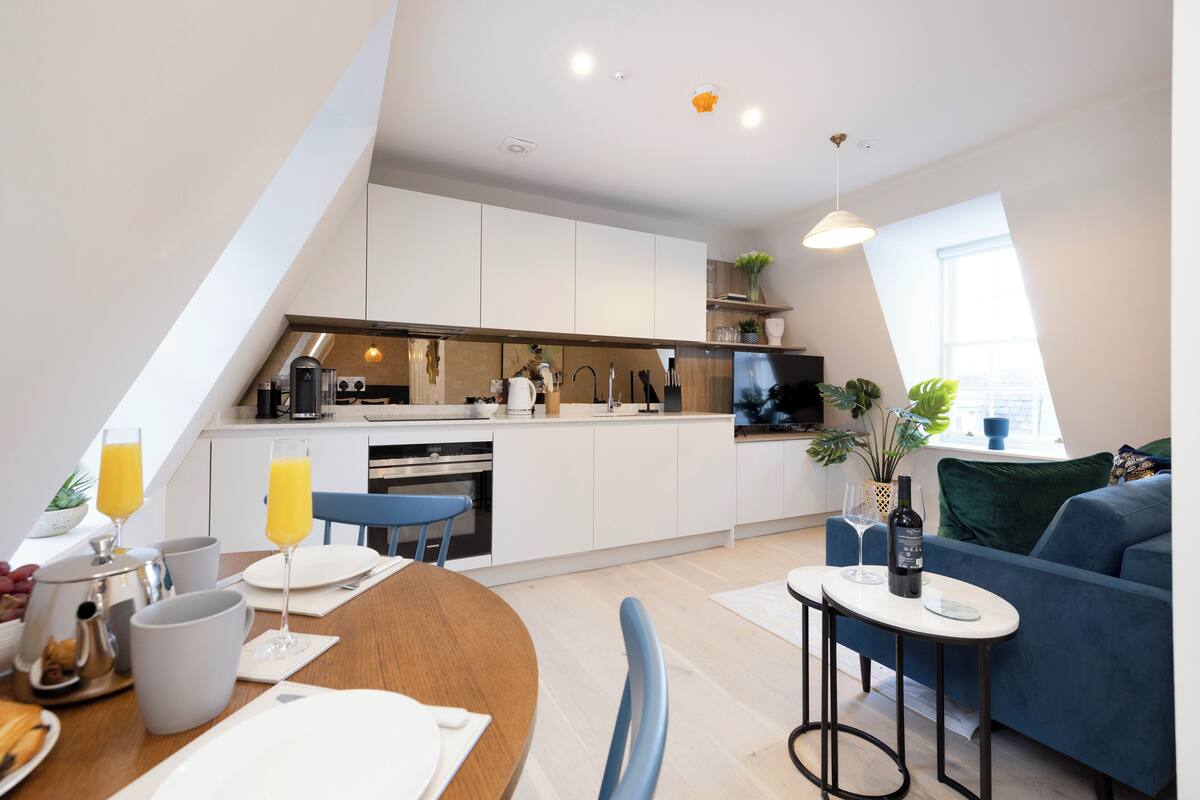 Una cocina moderna con armarios blancos, un comedor con mesa de madera y un sofá azul.